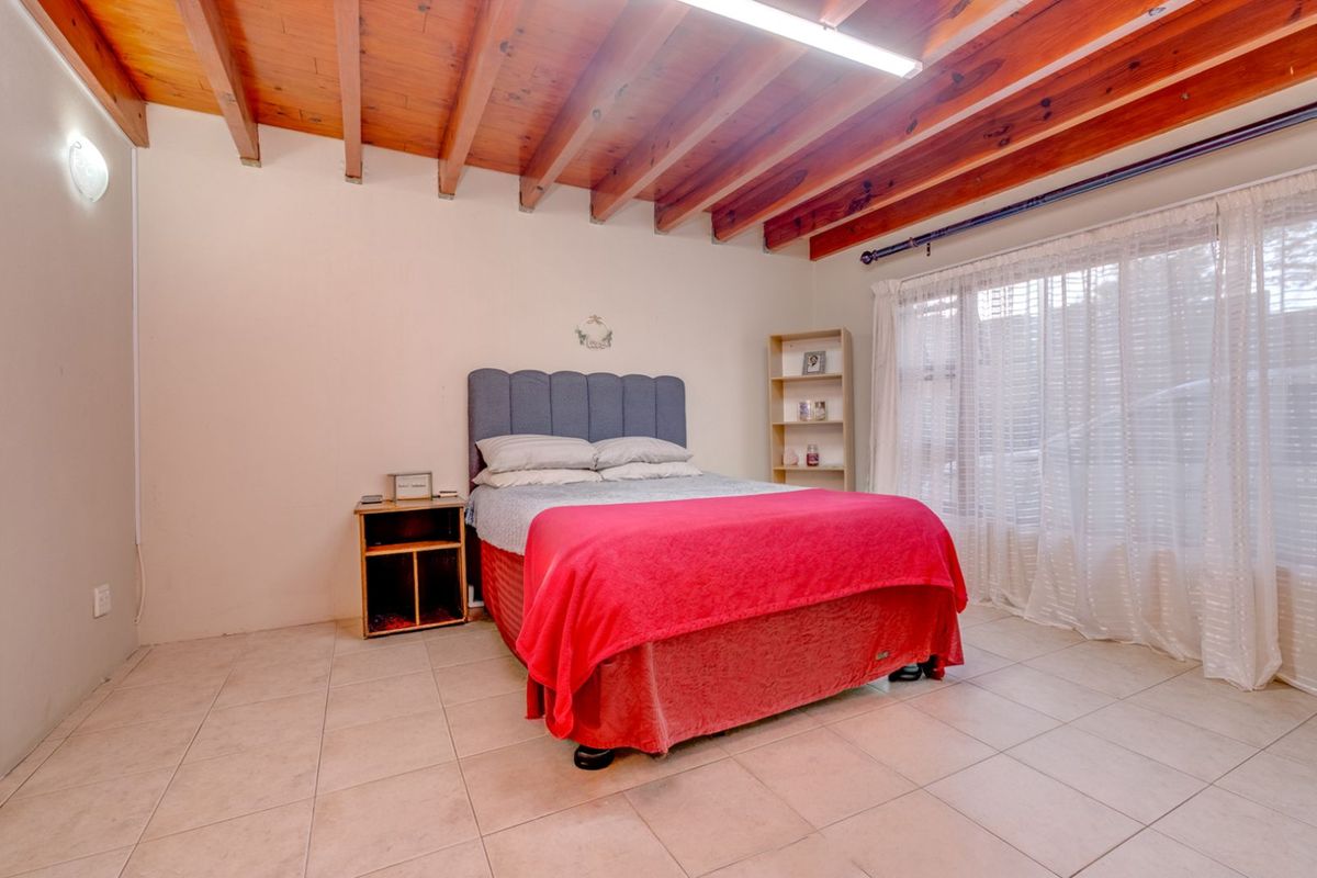 A bedroom featuring exposed timber ceiling beams, tiled flooring, and a large window with sheer curtains.