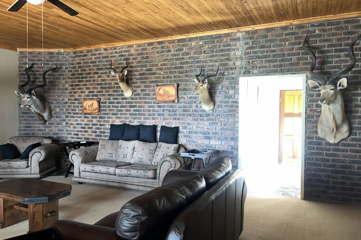 Spacious living room featuring a rustic exposed brick feature wall, timber-clad ceiling, and a ceiling fan, creating a warm and traditional farm-style atmosphere.