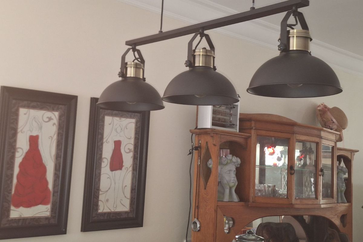 A close-up view of a three-light industrial-style pendant fixture suspended from the ceiling in a living area.