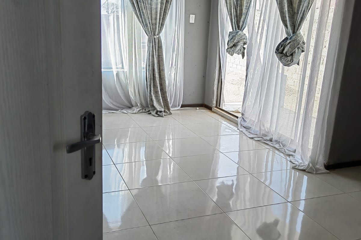 A bright, empty living room featuring large glass sliding doors, polished floor tiles, and a white tongue-and-groove ceiling.