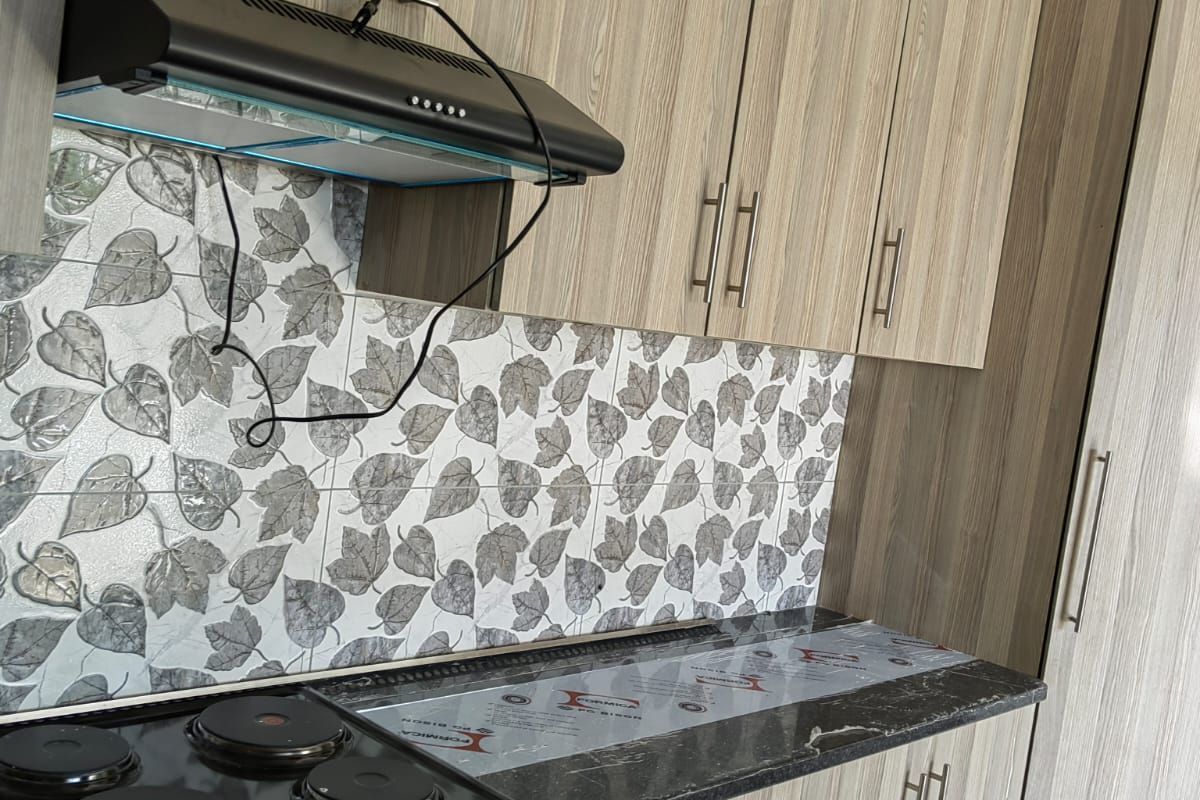 Modern kitchen featuring wood-grain cabinetry, dark stone-look countertops, a built-in electric stove, and a decorative leaf-patterned tiled backsplash.