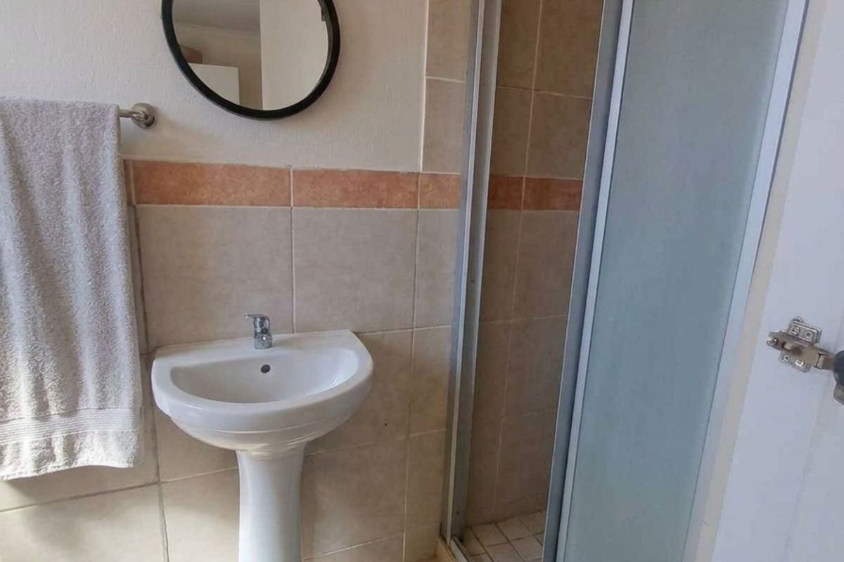 A functional bathroom featuring a pedestal basin, a shower enclosure with a sliding door, and neutral wall and floor tiling.