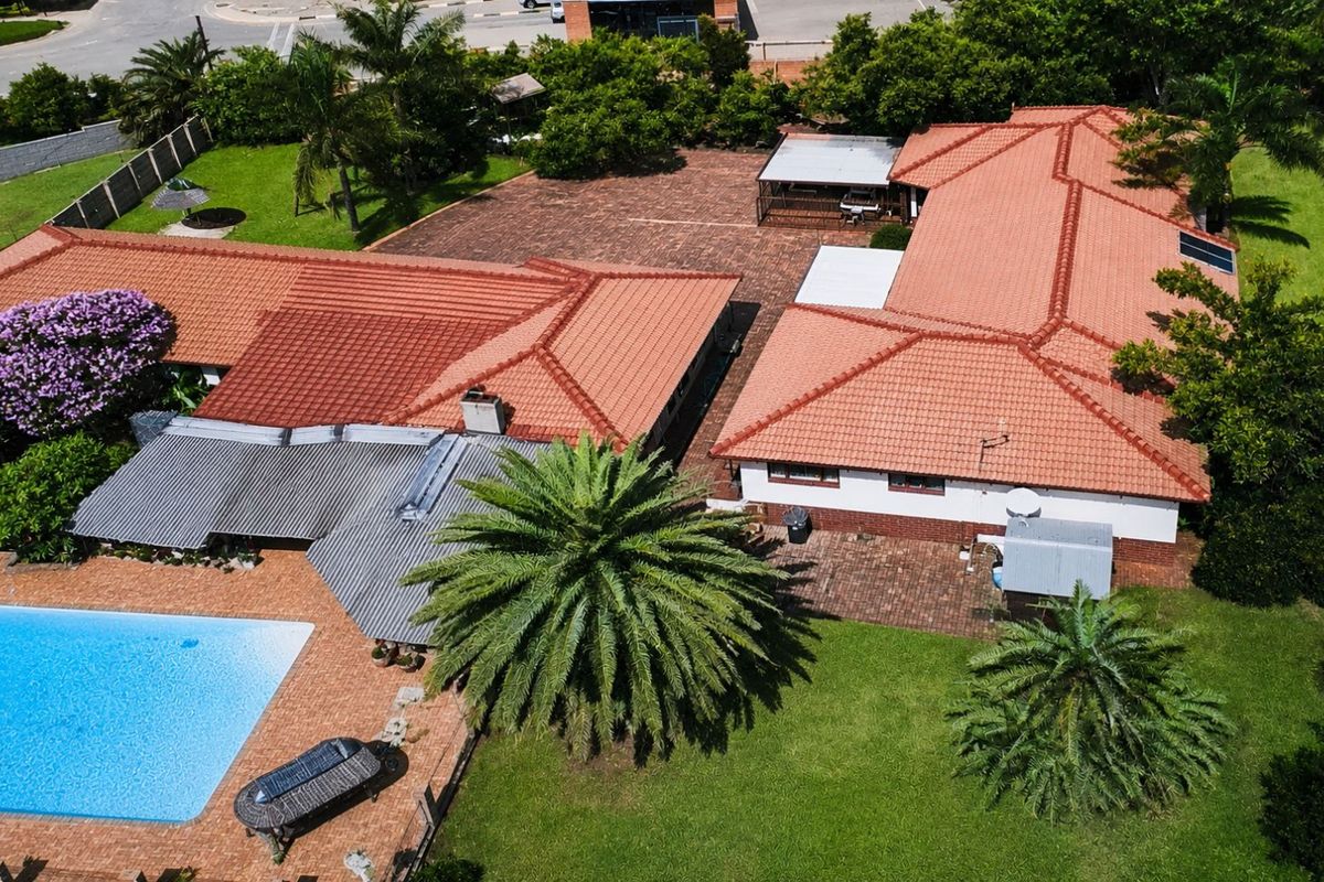 Aerial view of the property featuring a large swimming pool, expansive lawn, paved courtyard, and terracotta tiled roof structure.