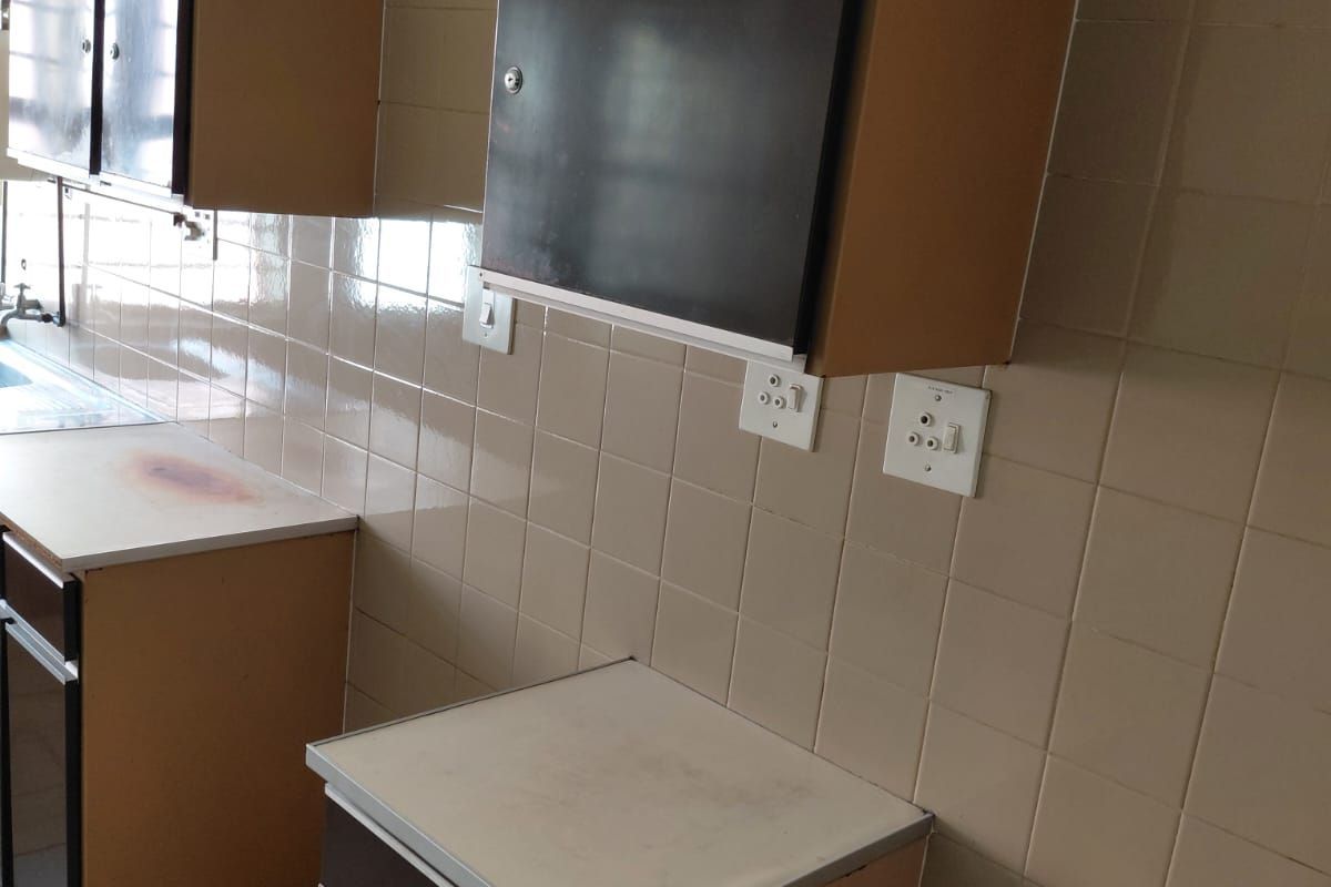 A dated kitchenette area featuring built-in cabinetry, tiled walls, and a sink, suitable for a small office utility space.
