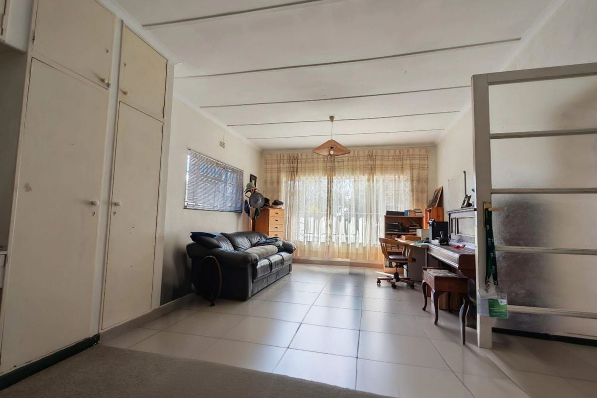A spacious living area featuring neutral floor tiles, built-in storage cupboards, and large windows allowing for ample natural light.