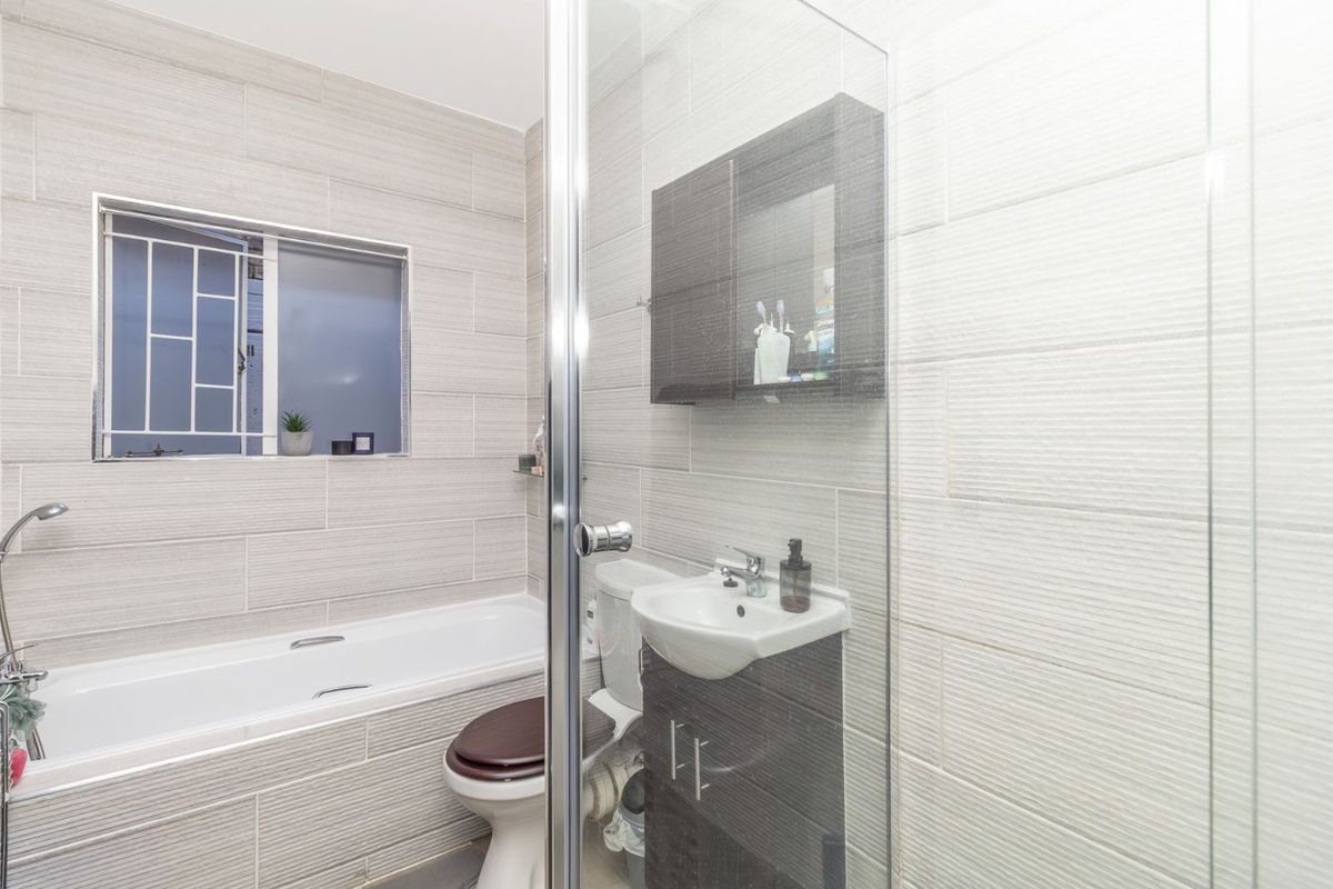 A modern bathroom featuring a tiled bathtub, a glass-enclosed shower, a wall-mounted vanity cabinet, and a toilet.