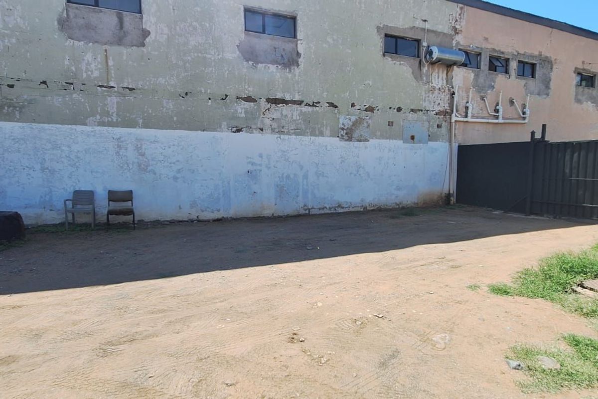 A rear exterior view of the property featuring a large unpaved yard area and a building facade showing significant signs of wear and weathering.