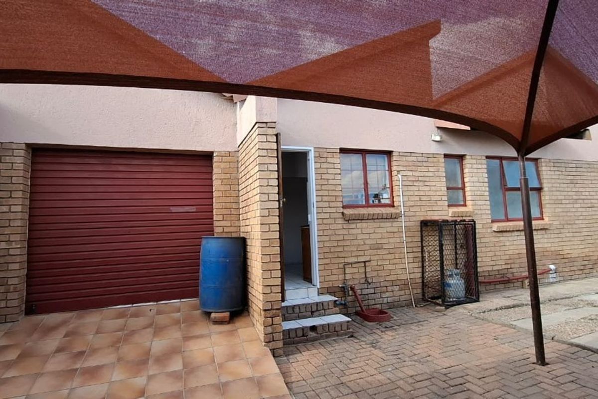 Rear exterior view featuring a brick facade, a roller garage door, tiled patio area, and a shade sail structure.