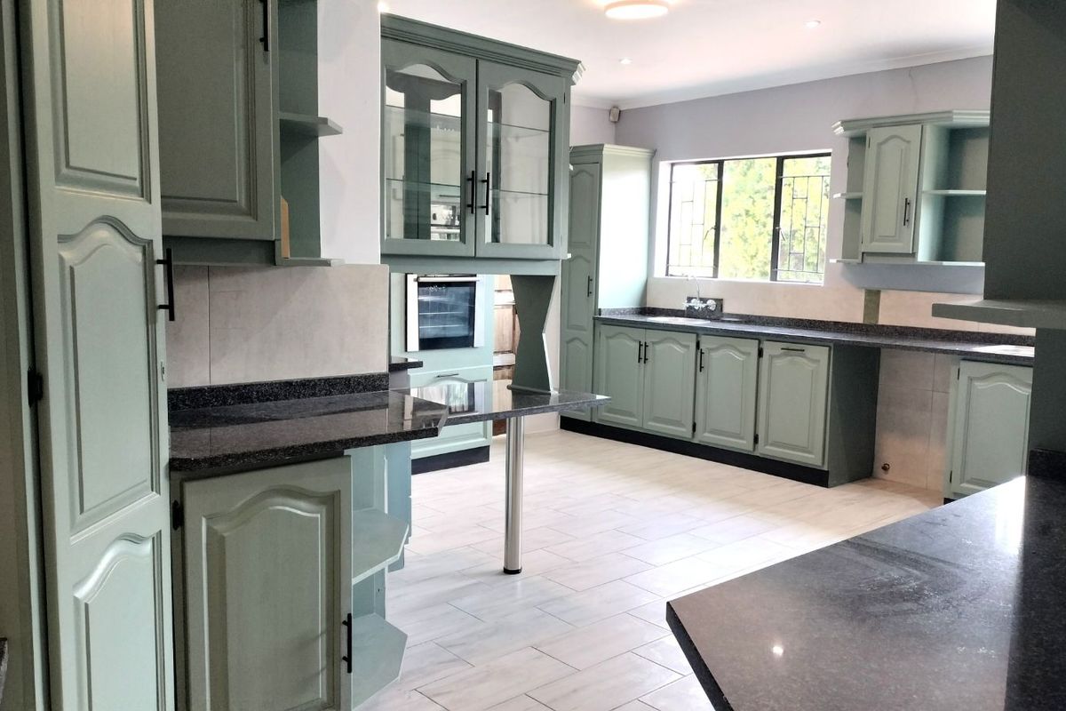 Spacious kitchen featuring sage green cabinetry, dark granite countertops, built-in oven, and light-toned tiled flooring with ample natural light.