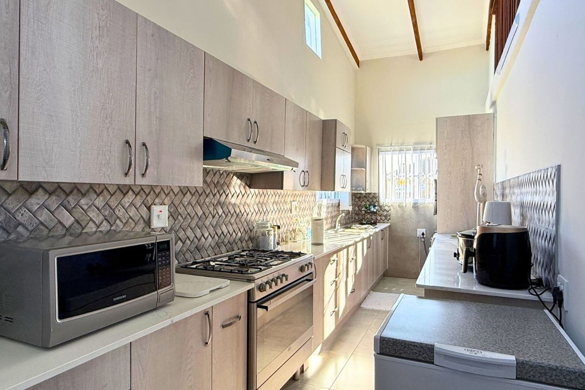 Modern kitchen featuring light wood-grain cabinetry, a gas stove with extractor fan, and a stylish herringbone-patterned tiled backsplash.