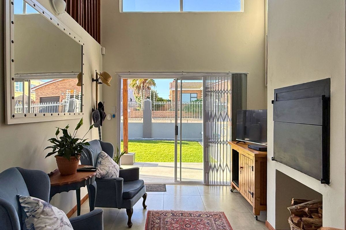 A bright living room featuring high ceilings, tiled flooring, a built-in fireplace, and sliding glass doors providing direct access to the rear garden.