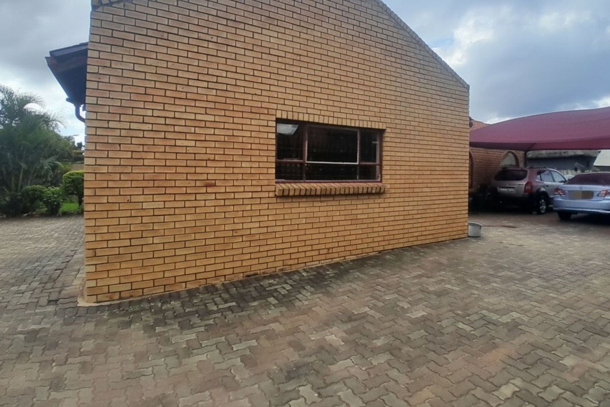 A side view of a face-brick residential building featuring a paved driveway and a covered carport area.