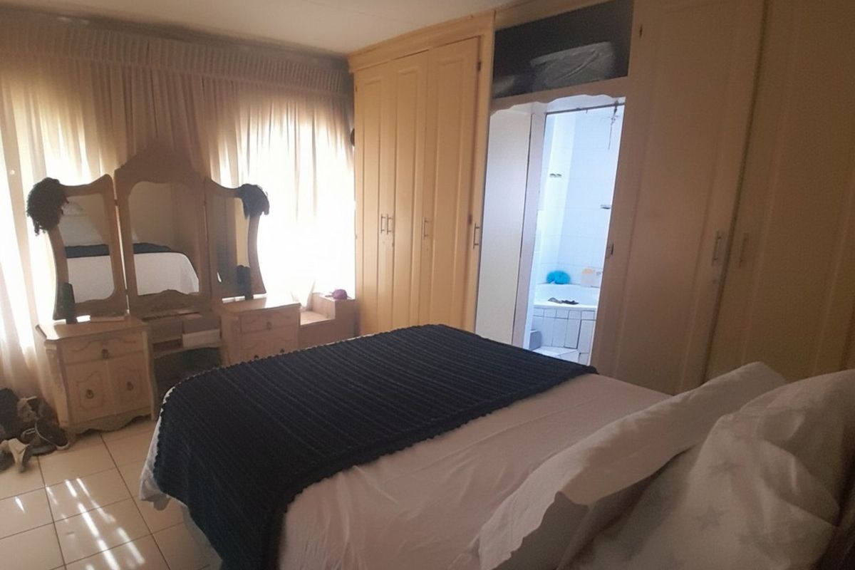 A bedroom featuring built-in wardrobes and tiled flooring, with an adjoining en-suite bathroom visible through the doorway.