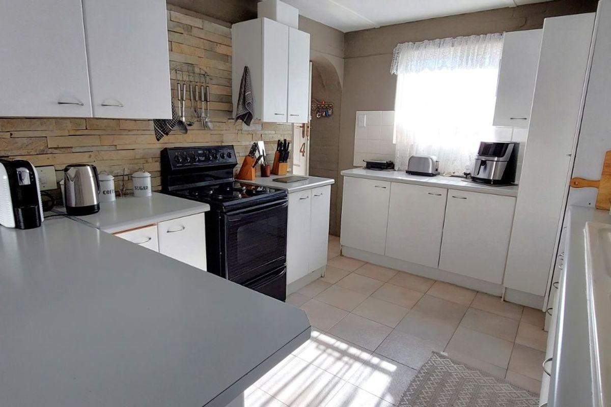 A functional kitchen featuring white cabinetry, a stone-cladding backsplash, tiled flooring, and a freestanding stove, offering a practical layout for daily meal preparation.