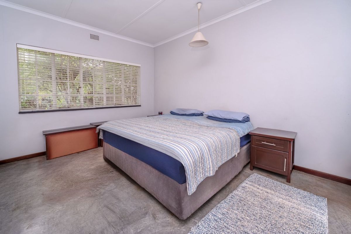 A bedroom featuring polished concrete flooring, a large window with fitted blinds, and a simple pendant light fixture.