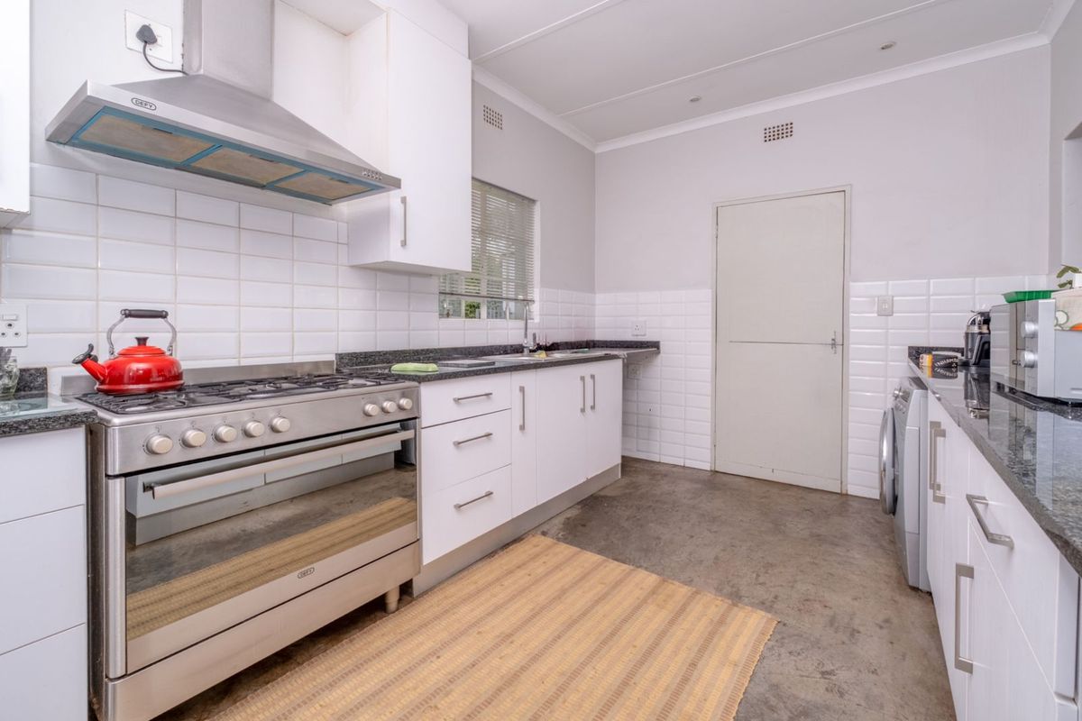 A functional kitchen featuring white cabinetry, granite countertops, a stainless steel gas stove with extractor fan, and tiled splashbacks.