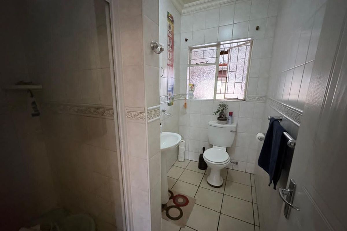 A functional bathroom featuring a pedestal basin, toilet, and a shower enclosure with tiled walls and flooring.