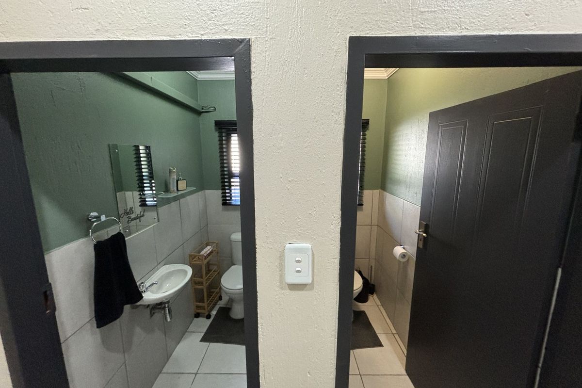 A view into two adjacent office restrooms featuring tiled lower walls, wall-mounted basins, and toilets with dark-framed doorways.