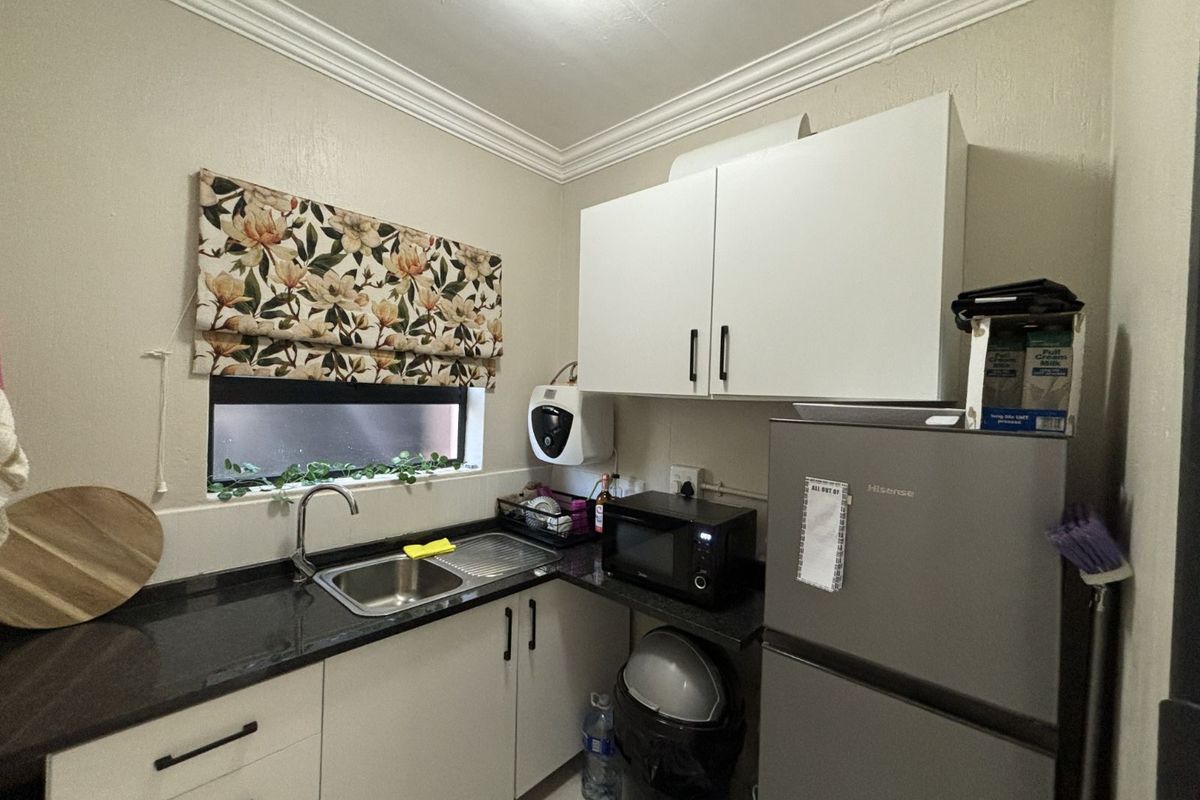 Compact kitchenette featuring dark granite countertops, stainless steel sink, and white cabinetry with modern black hardware.