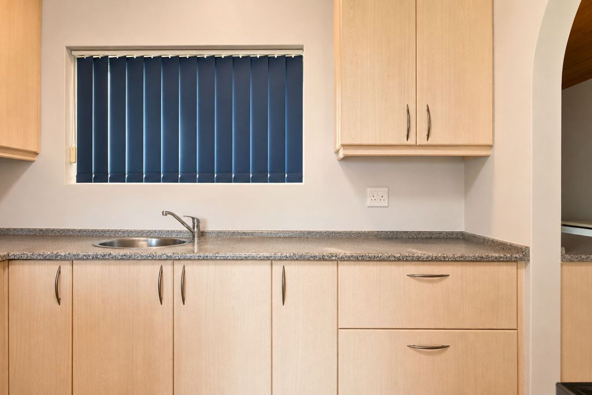 A functional kitchen area featuring light wood cabinetry, granite-look countertops, and a stainless steel sink.