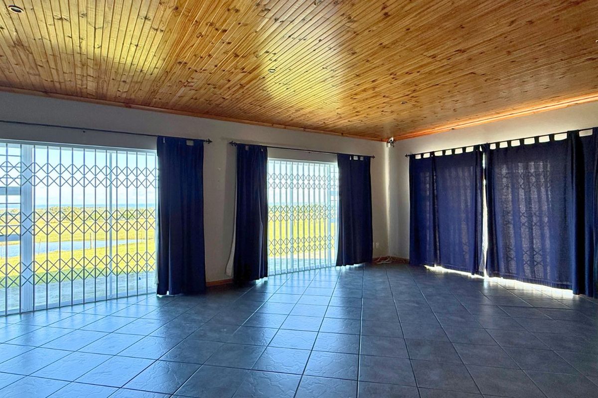 Spacious living area featuring tiled flooring, timber-clad ceiling, and multiple sliding glass doors with security gates providing access to the exterior.