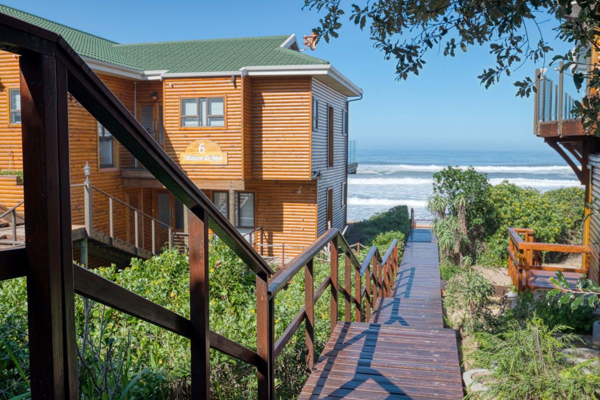 A wooden staircase leads down towards the beach, offering direct access from the coastal property with its distinctive log-style exterior cladding.