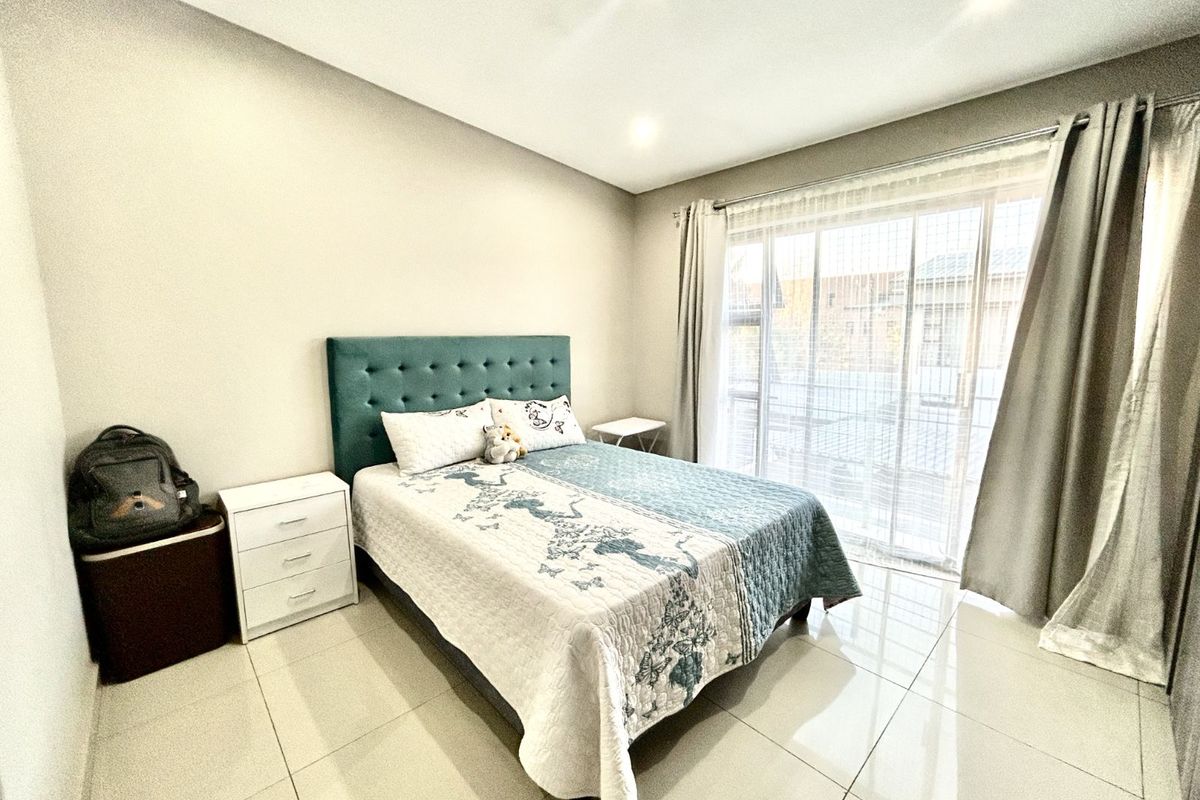 A bright and modern bedroom featuring large glass sliding doors with curtains, recessed ceiling lighting, and polished floor tiles.
