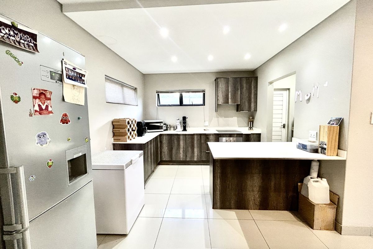 Modern kitchen featuring dark wood-grain cabinetry, white countertops, tiled flooring, recessed ceiling lighting, and a functional breakfast bar layout.