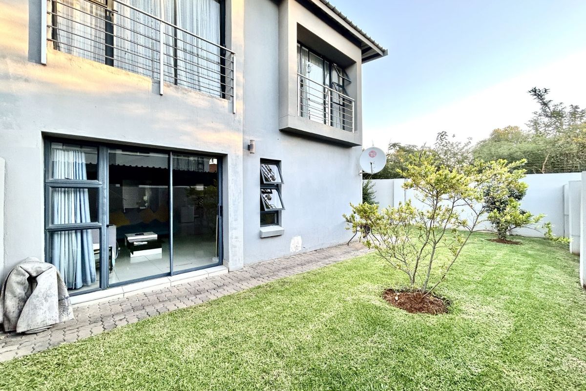Rear view of the townhouse featuring a private garden, paved walkway, and sliding glass doors leading into the living area.