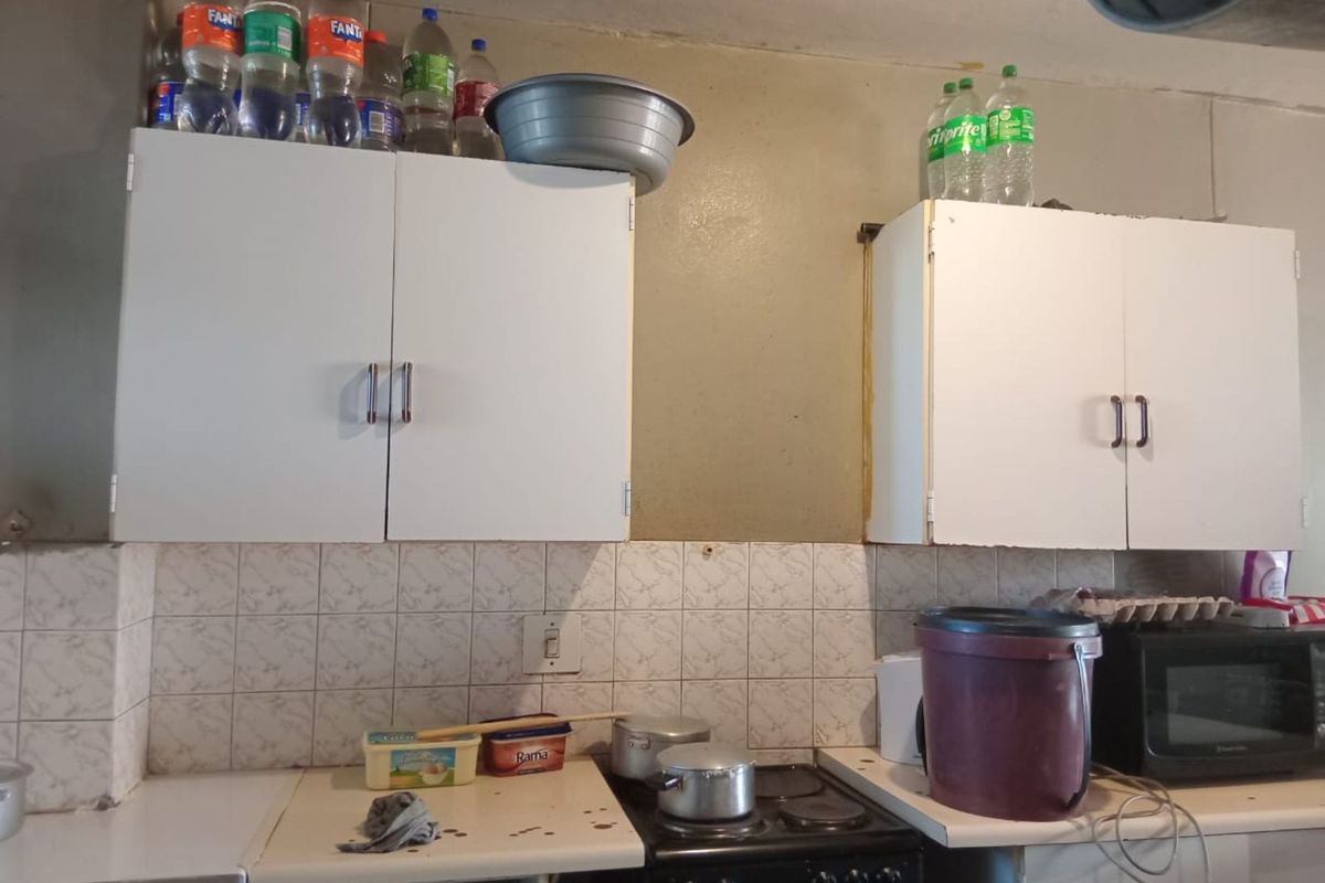 A functional kitchen area featuring white wall-mounted cabinetry, tiled splashbacks, and a built-in stove, offering a practical layout for daily meal preparation.