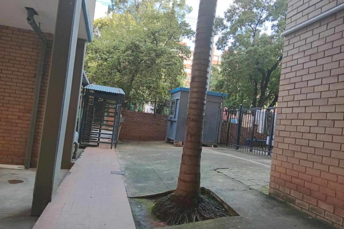 An outdoor courtyard area featuring brick walls, paved pathways, and a central tree, providing a functional communal space within the apartment complex.