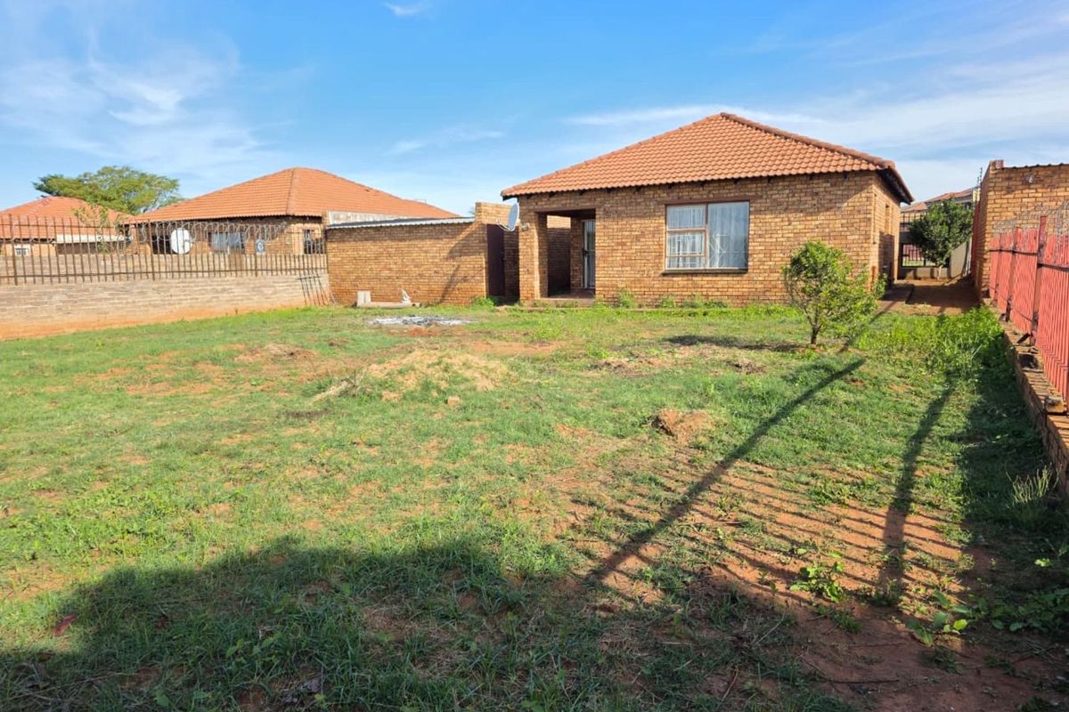 A view of the rear exterior of the house, featuring a brick facade, tiled roof, and a spacious backyard enclosed by perimeter walls.
