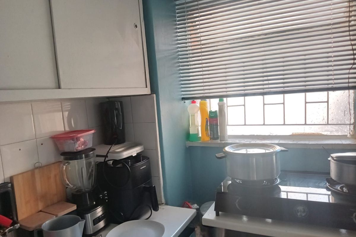 A compact kitchen area featuring built-in cabinetry, tiled splashbacks, and a window with fitted blinds, providing functional food preparation space.