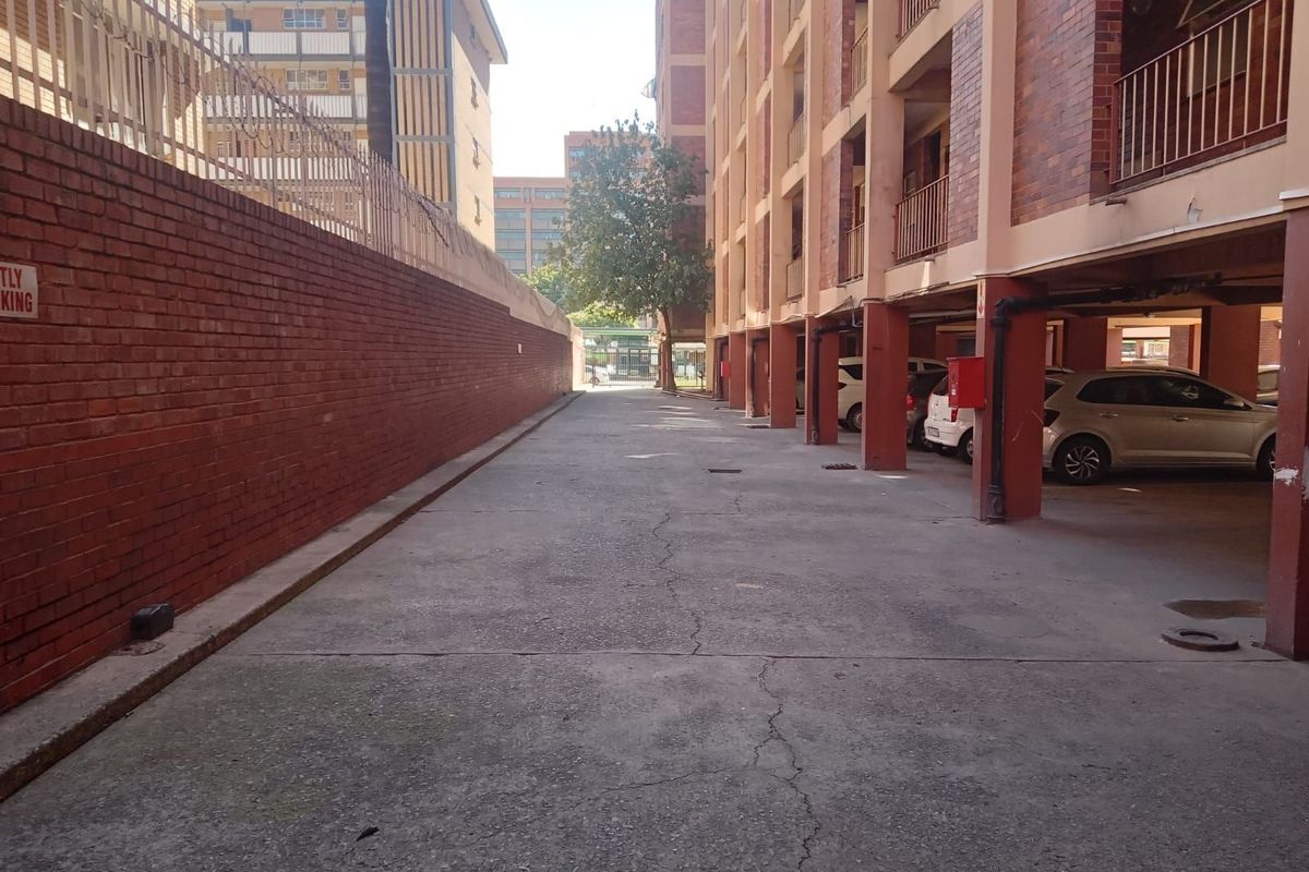 Exterior view of the apartment complex parking area featuring covered parking bays and a brick boundary wall.
