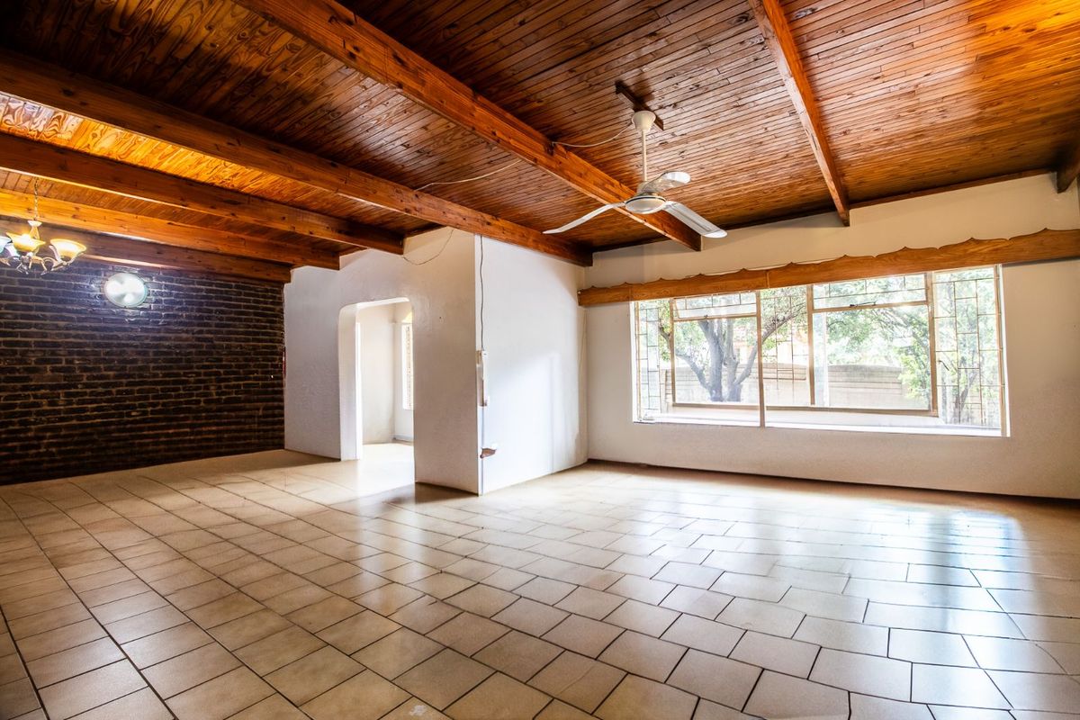 Spacious living area featuring a vaulted timber-beamed ceiling, exposed brick feature wall, and large windows providing natural light.