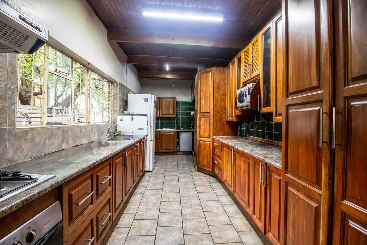 A functional galley-style kitchen featuring extensive timber cabinetry, stone-look laminate countertops, tiled splashbacks, and a timber-beamed ceiling.