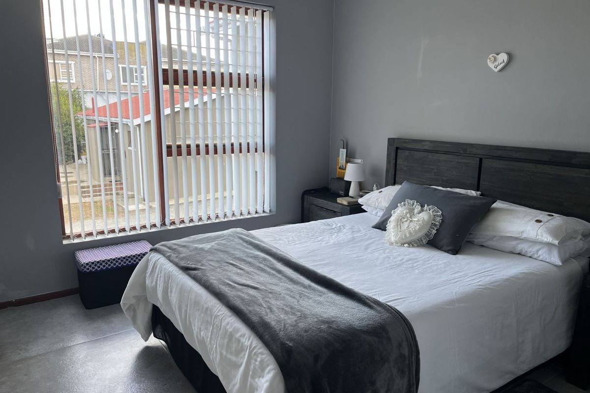 A bedroom featuring large windows with vertical blinds, tiled flooring, and neutral wall tones, offering a functional and comfortable living space.