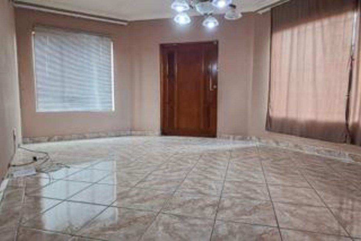 A spacious, empty living area featuring tiled flooring, a solid wood entrance door, and large windows with fitted blinds.