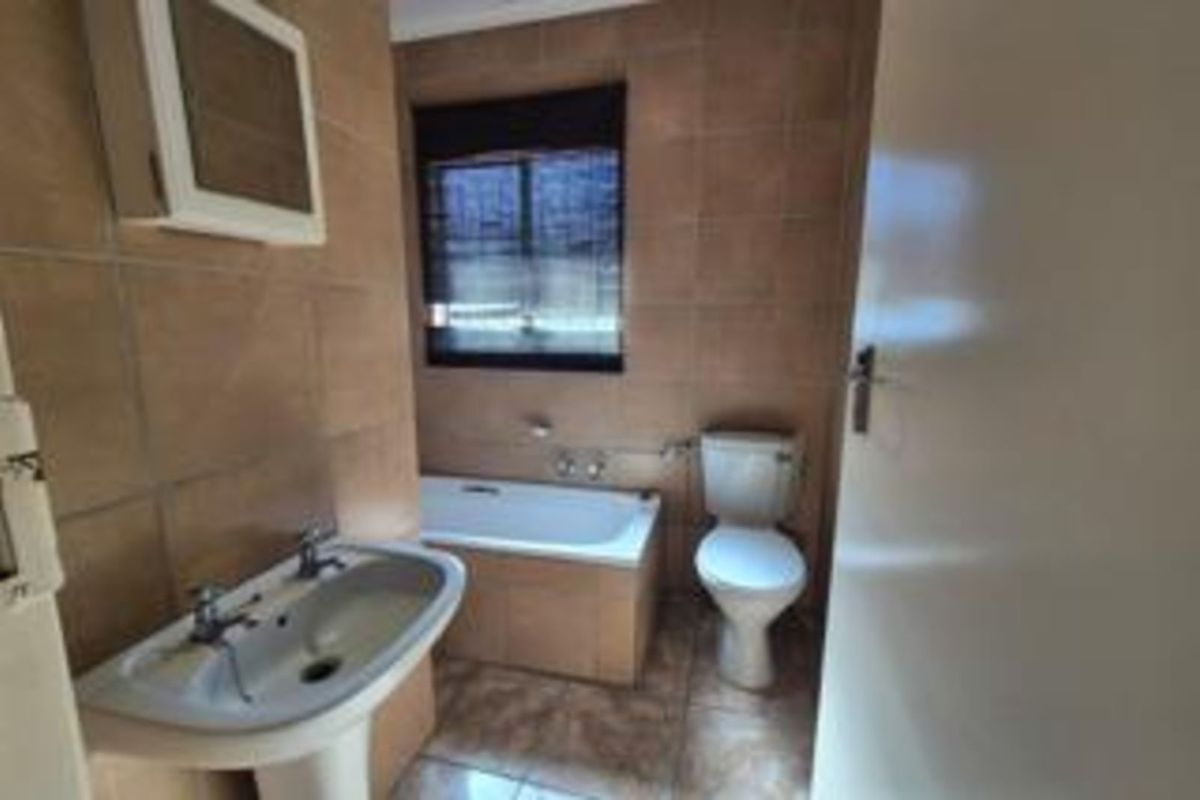 A functional bathroom featuring a pedestal basin, a built-in bathtub, and a standard toilet with full-height wall tiling.