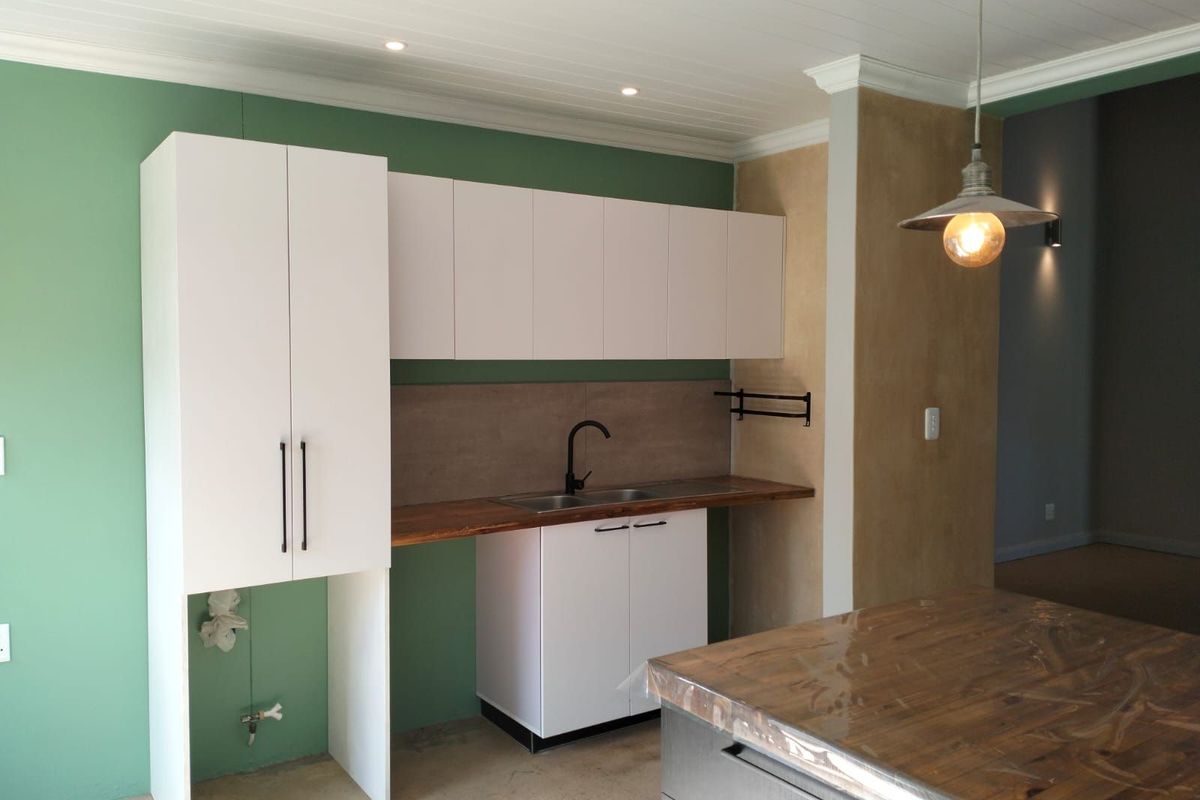 A compact kitchen area featuring white cabinetry, a wooden countertop, a modern black faucet, and a central island with a wooden top.