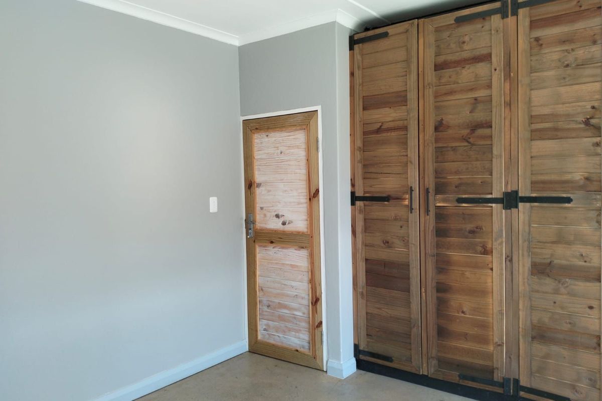 A clean interior space featuring built-in wooden cabinetry and a rustic timber door, set against neutral grey walls and polished concrete flooring.