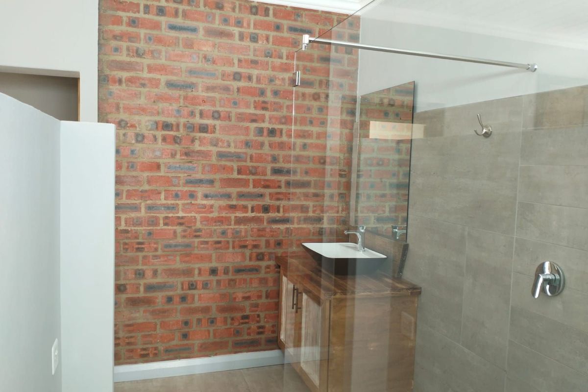 Modern bathroom featuring a striking exposed brick feature wall, a floating wooden vanity with a vessel sink, and a glass-enclosed walk-in shower.