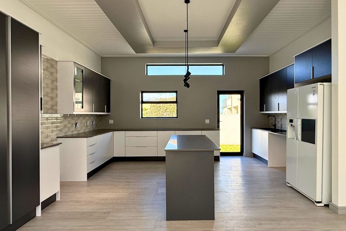 Modern kitchen featuring a central island, two-tone cabinetry, stone countertops, recessed tray ceiling, and direct access to the exterior.