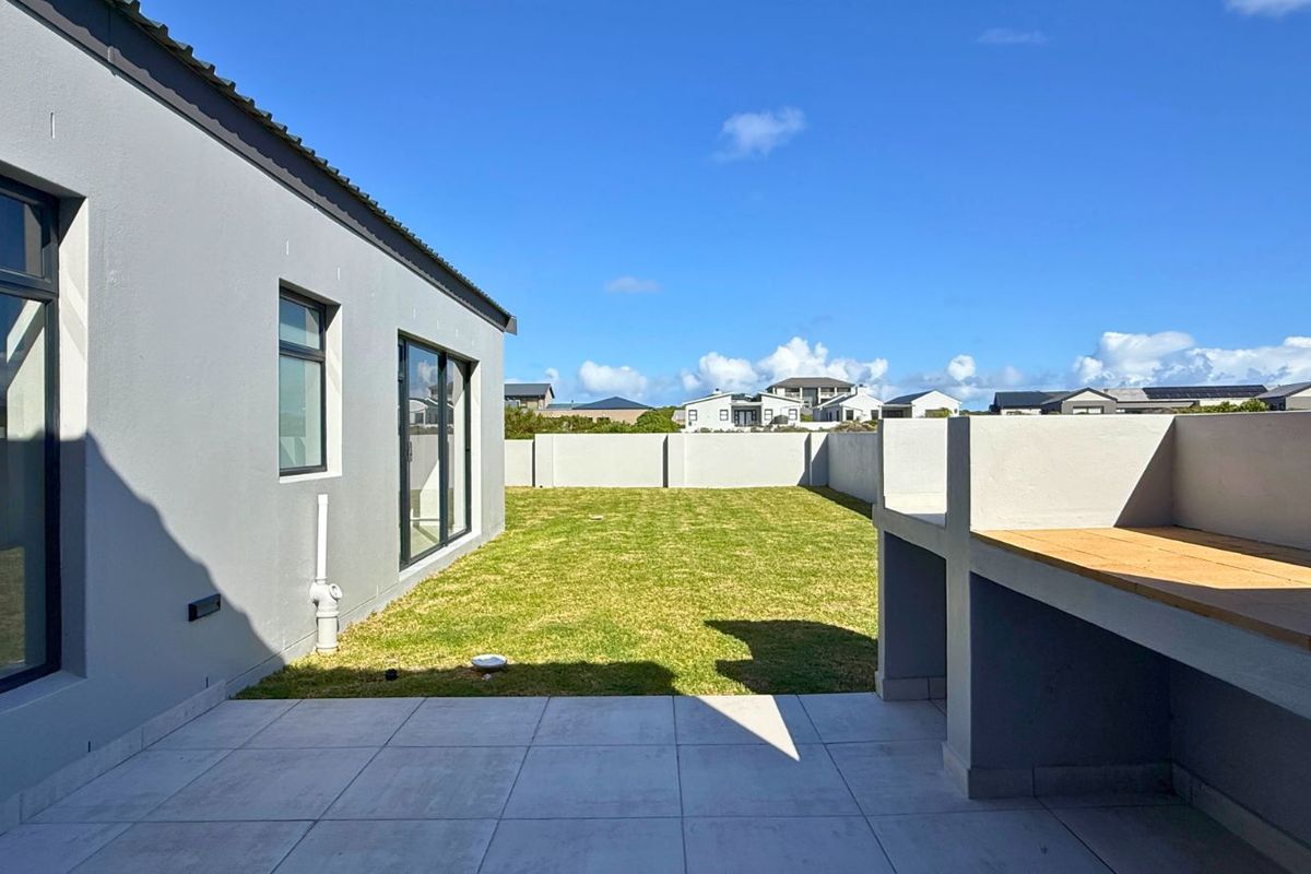 A well-maintained rear garden featuring a paved patio area with a built-in braai, overlooking a level lawn enclosed by perimeter walls.