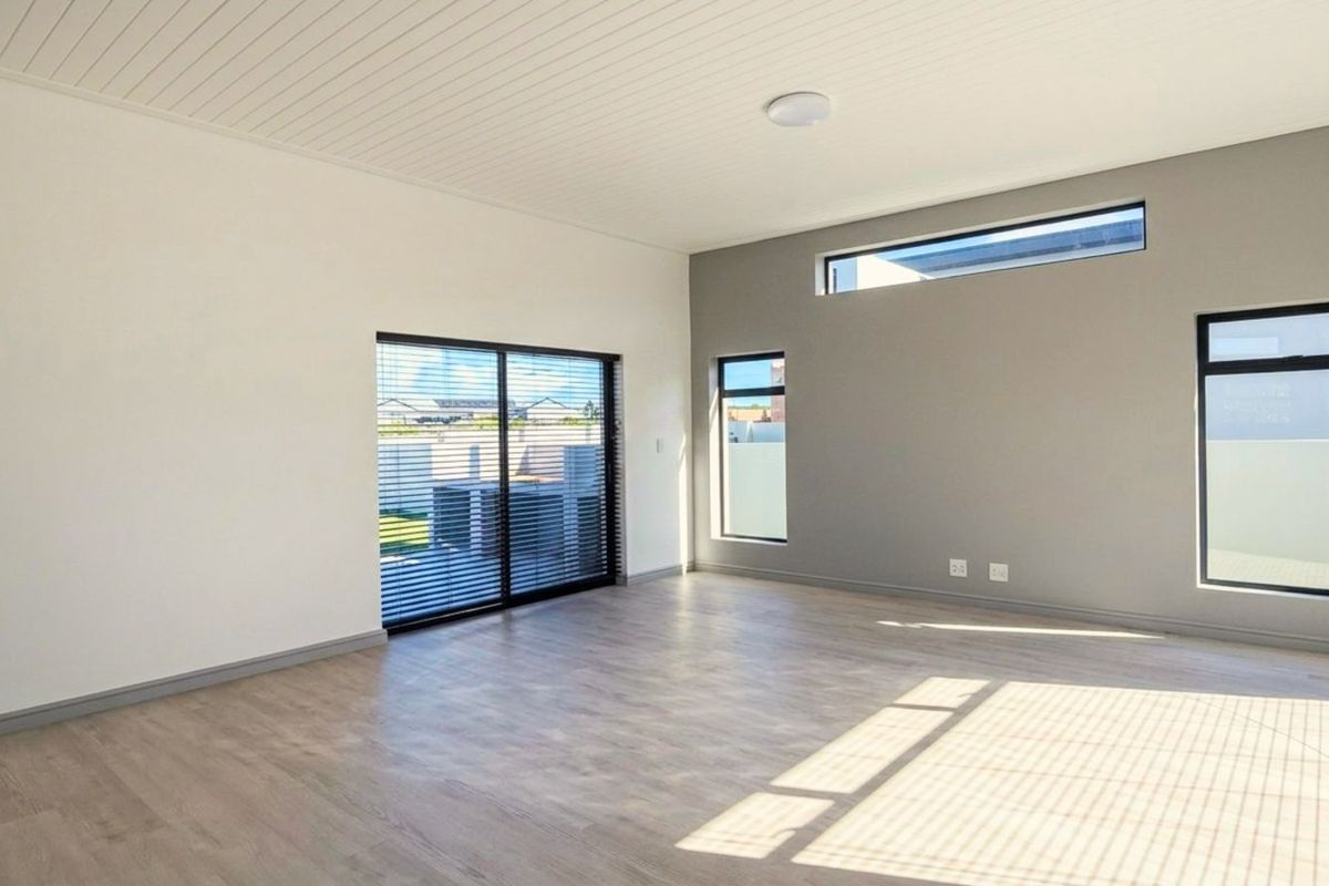 A bright, modern living area featuring neutral tones, wood-look flooring, high ceilings, and large windows that provide ample natural light.