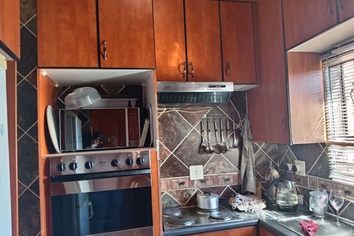 Compact kitchen featuring wood-finish cabinetry, built-in oven, extractor fan, and a tiled backsplash with integrated sink and hob.