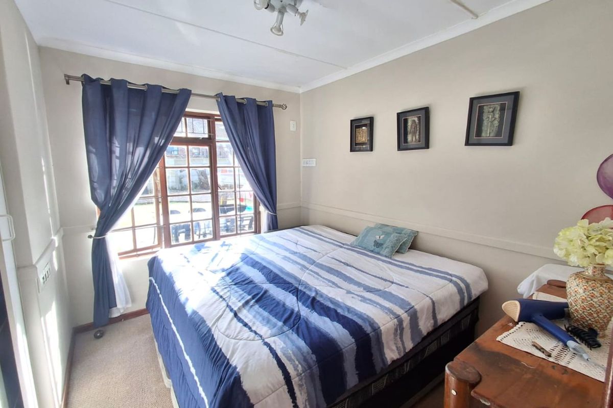 A functional bedroom featuring a large window with natural light, neutral wall finishes, and carpeted flooring.