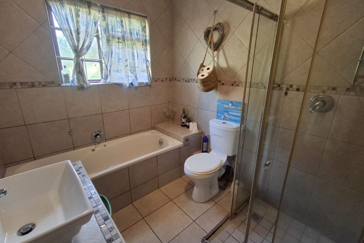 A functional bathroom featuring a tiled bathtub, separate glass-enclosed shower, toilet, and a vanity basin with mosaic tile detailing.