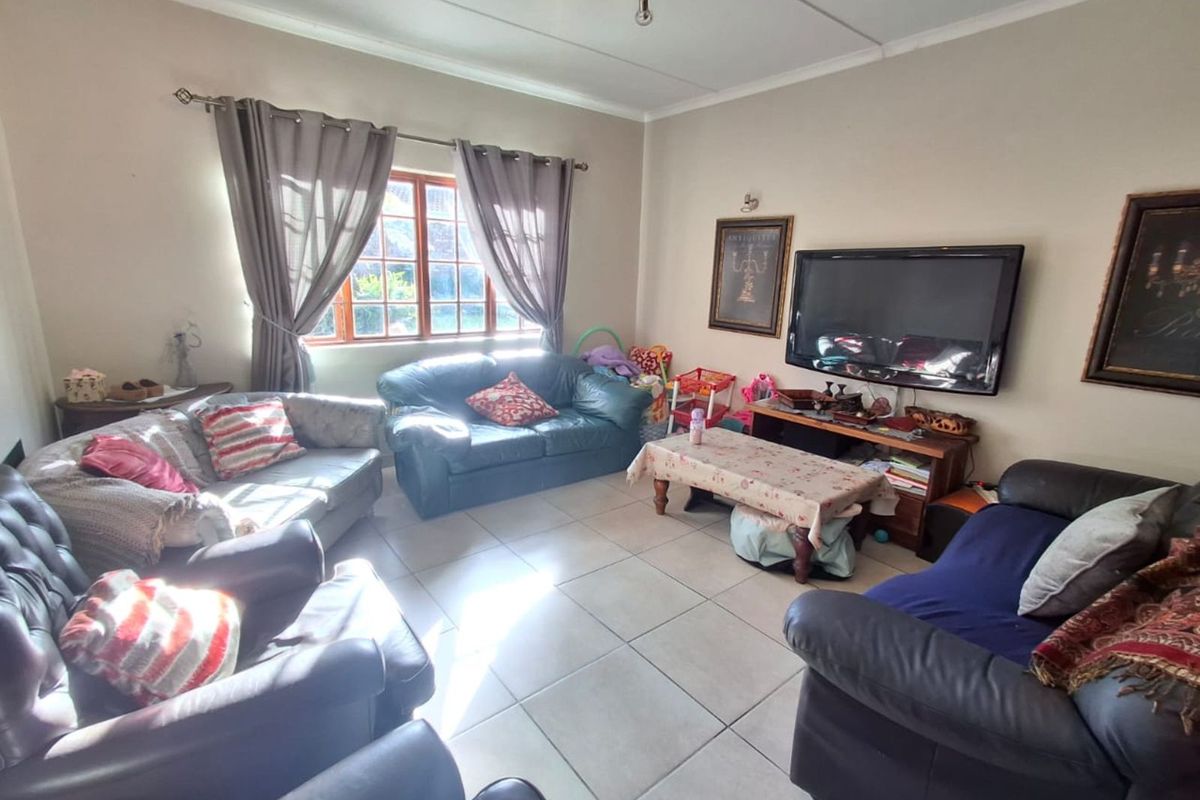 A spacious living room featuring large ceramic floor tiles, a window with curtain rods, and a wall-mounted television setup.