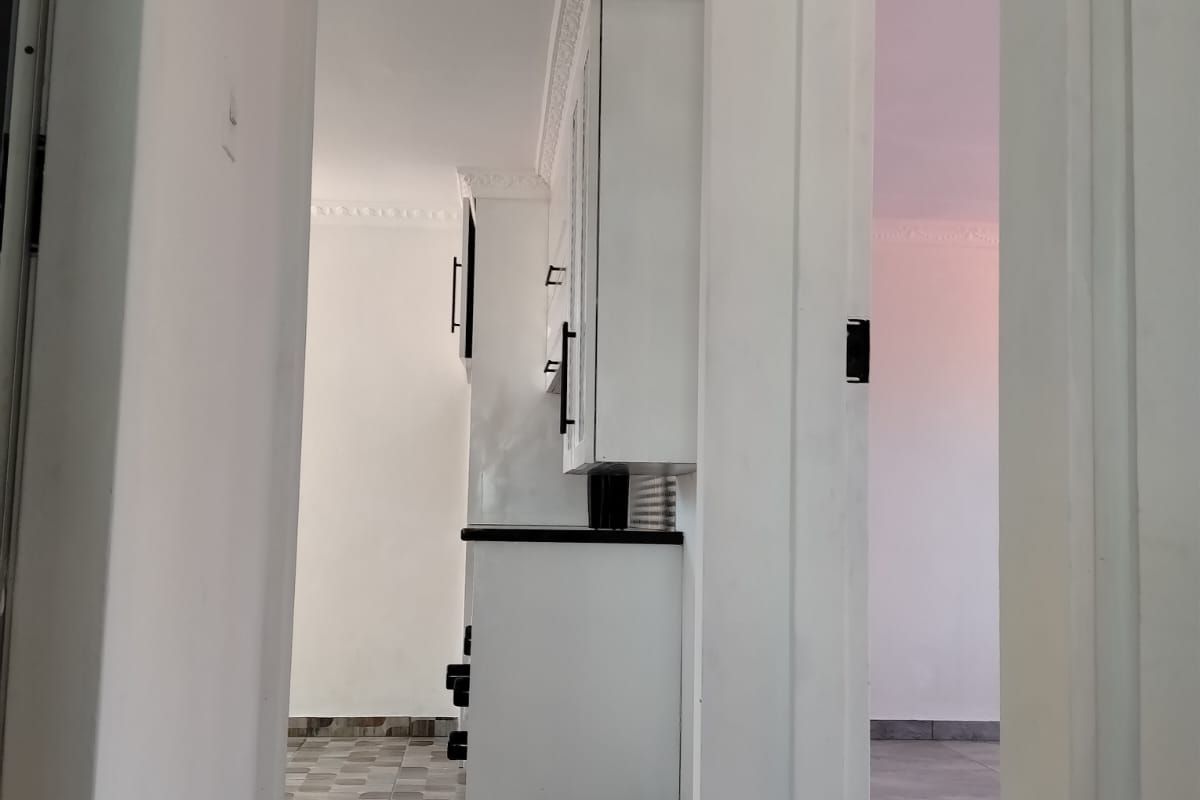 A view through a doorway into a kitchen area featuring white cabinetry, dark countertops, and tiled flooring.